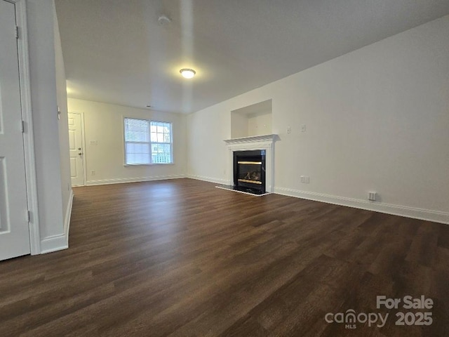 unfurnished living room featuring a premium fireplace, dark wood finished floors, and baseboards