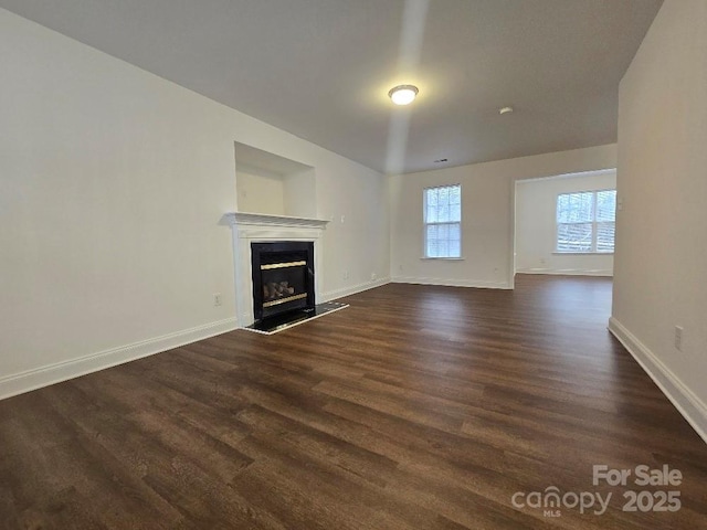 unfurnished living room featuring baseboards, dark wood-style flooring, and a glass covered fireplace