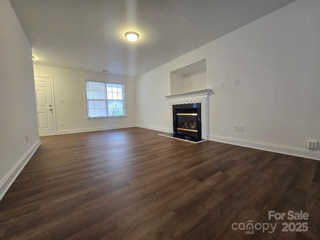 unfurnished living room with dark wood finished floors, a high end fireplace, and baseboards