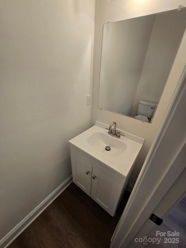 half bath featuring vanity, baseboards, and wood finished floors