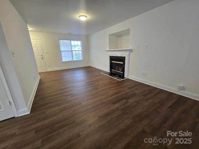 unfurnished living room featuring dark wood-type flooring, a glass covered fireplace, and baseboards