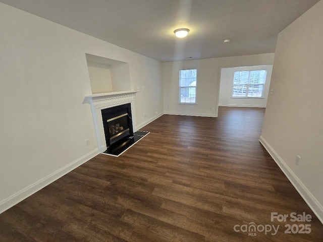 unfurnished living room with a glass covered fireplace, dark wood-style flooring, and baseboards