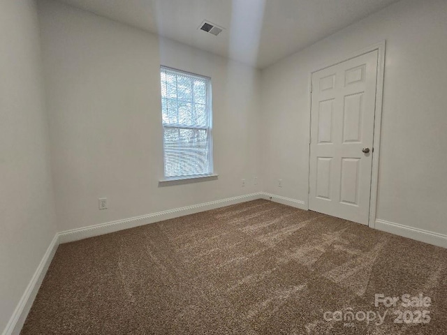 spare room with dark colored carpet, visible vents, and baseboards