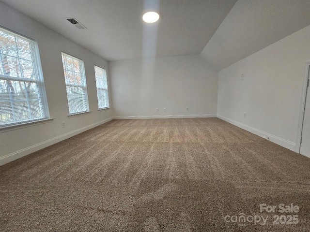 unfurnished room featuring carpet floors, baseboards, visible vents, and vaulted ceiling