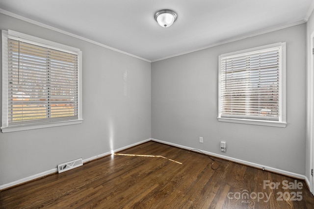 empty room with ornamental molding, wood finished floors, visible vents, and baseboards