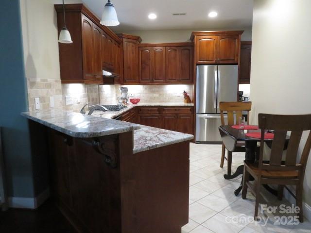 kitchen featuring hanging light fixtures, a peninsula, tasteful backsplash, and appliances with stainless steel finishes