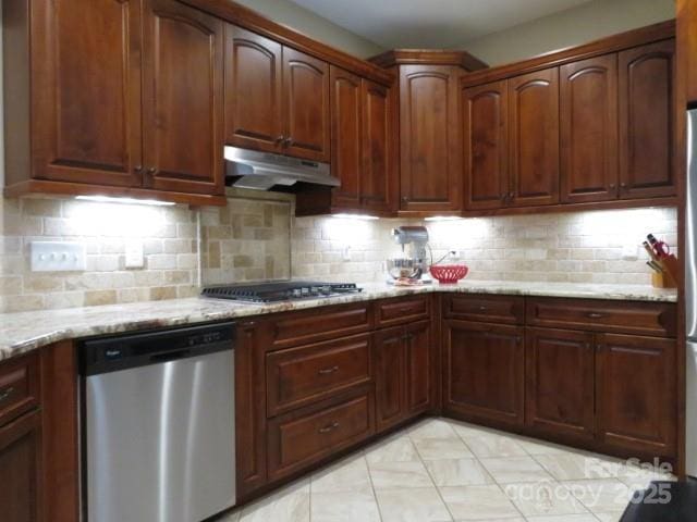 kitchen with under cabinet range hood, stainless steel appliances, light stone countertops, and tasteful backsplash