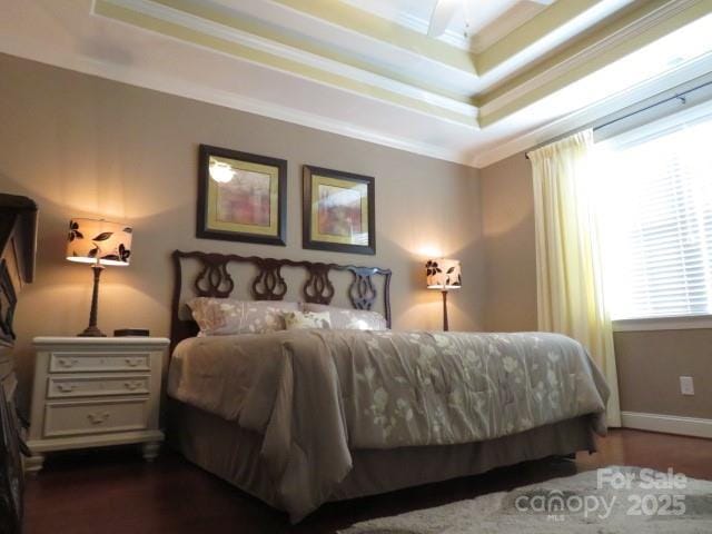 bedroom with a raised ceiling, crown molding, dark wood-style flooring, and baseboards