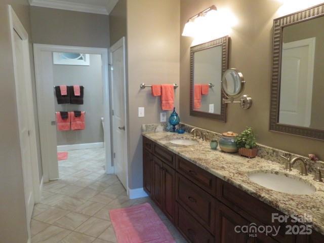 full bath with double vanity, ornamental molding, baseboards, and a sink