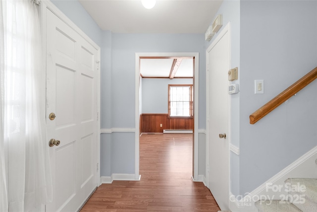 hall with a baseboard heating unit, stairs, wood finished floors, and wainscoting