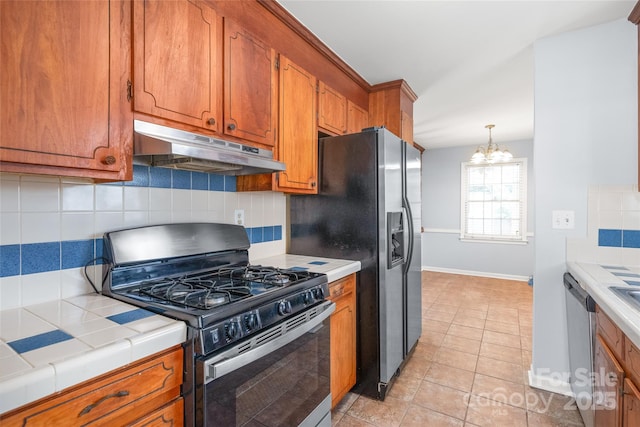 kitchen with gas stove, tile counters, under cabinet range hood, dishwasher, and brown cabinets