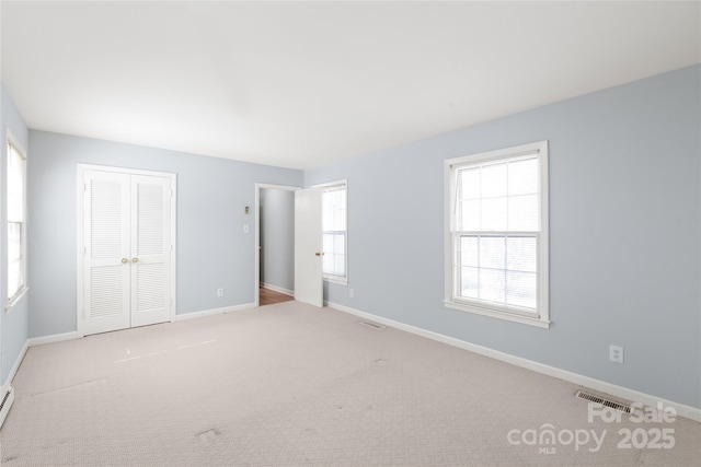 unfurnished bedroom featuring baseboard heating, baseboards, visible vents, and a closet