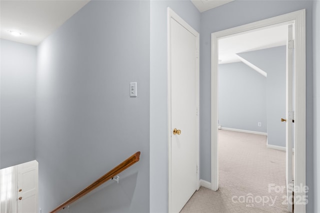 hallway with an upstairs landing, light colored carpet, and baseboards