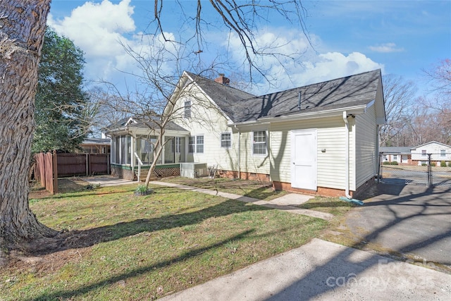 rear view of property with fence, roof with shingles, a yard, a sunroom, and a chimney