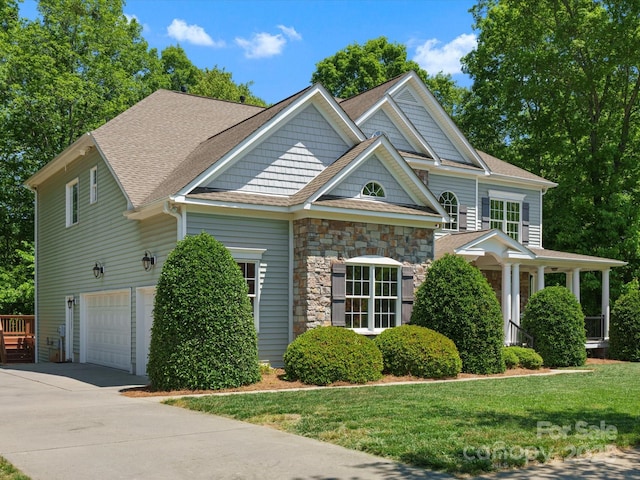 view of front of property with driveway, a garage, a front lawn, a shingled roof, and stone siding