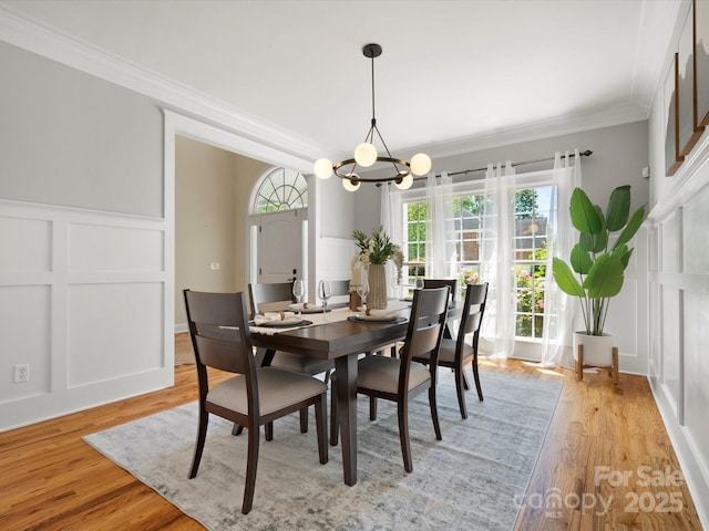 dining space with ornamental molding, a decorative wall, light wood-type flooring, and a notable chandelier