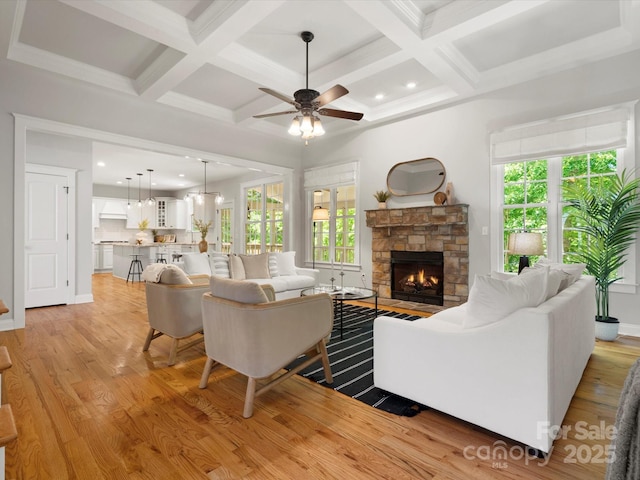 living room with a healthy amount of sunlight, ceiling fan, coffered ceiling, and a stone fireplace
