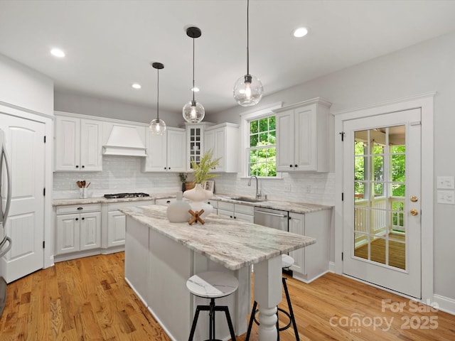 kitchen featuring stainless steel gas cooktop, white cabinets, a sink, and custom range hood