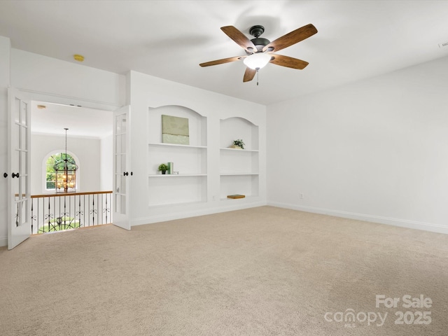 unfurnished room with light carpet, built in features, ceiling fan with notable chandelier, baseboards, and visible vents