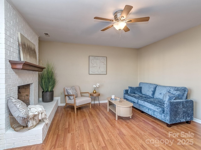 living area with ceiling fan, a fireplace, visible vents, baseboards, and light wood finished floors