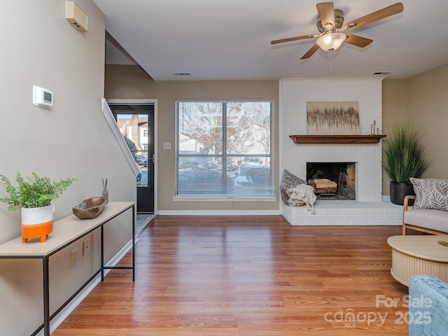 living area featuring light wood finished floors, ceiling fan, a fireplace, and visible vents