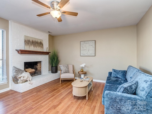 living area featuring visible vents, a ceiling fan, a brick fireplace, wood finished floors, and baseboards