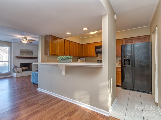 kitchen with light countertops, a brick fireplace, light wood-type flooring, black appliances, and brown cabinetry