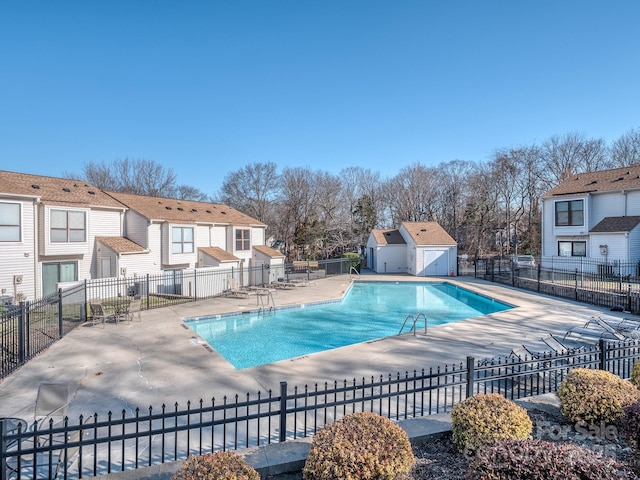 community pool with a patio area, fence, and an outdoor structure