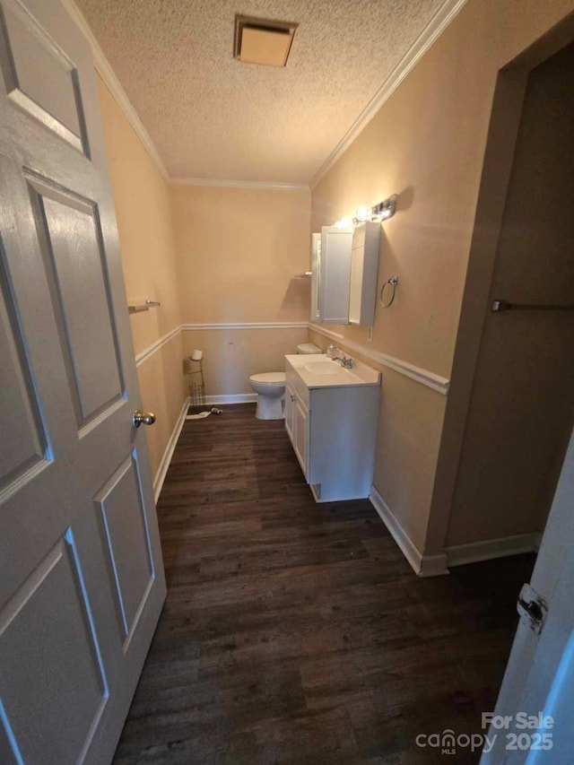 half bathroom with vanity, wood finished floors, ornamental molding, a textured ceiling, and toilet