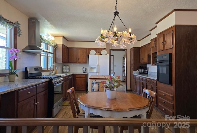 kitchen with decorative backsplash, gas range, range hood, white fridge with ice dispenser, and black oven