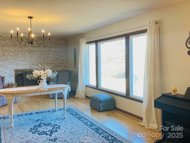 office space featuring an inviting chandelier, a textured ceiling, brick wall, wood finished floors, and baseboards