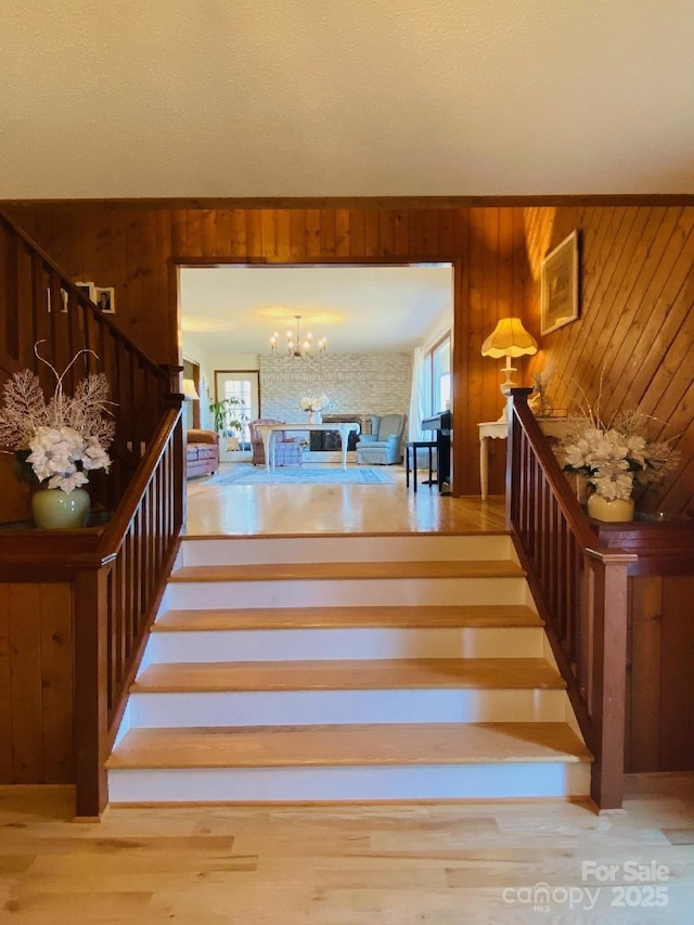 stairs with wood finished floors, wood walls, and an inviting chandelier