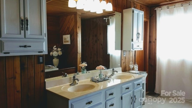 full bathroom with double vanity, wood walls, a sink, and an inviting chandelier