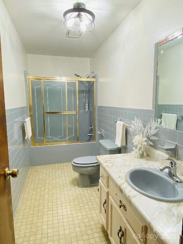 full bathroom with wainscoting, toilet, combined bath / shower with glass door, vanity, and tile walls