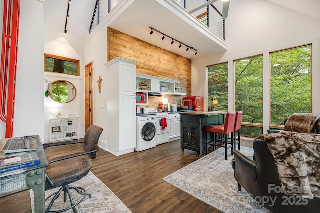 kitchen with dark wood finished floors, white stove, a towering ceiling, white cabinets, and washer / clothes dryer