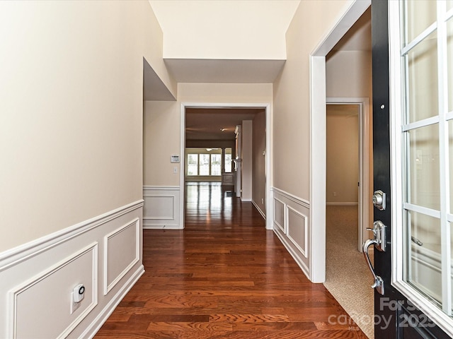 hallway with dark wood finished floors, a decorative wall, and a wainscoted wall