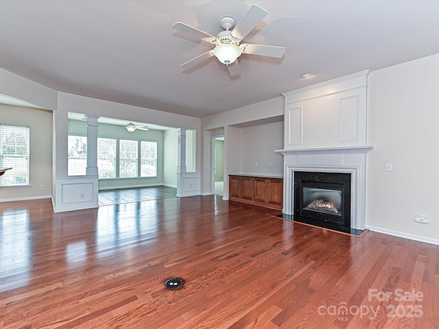 unfurnished living room featuring wood finished floors, a wealth of natural light, a ceiling fan, and ornate columns