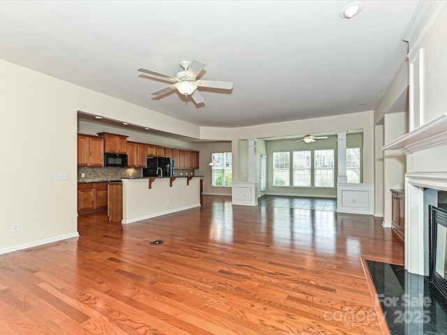 unfurnished living room featuring a ceiling fan, light wood-style floors, a premium fireplace, baseboards, and ornate columns