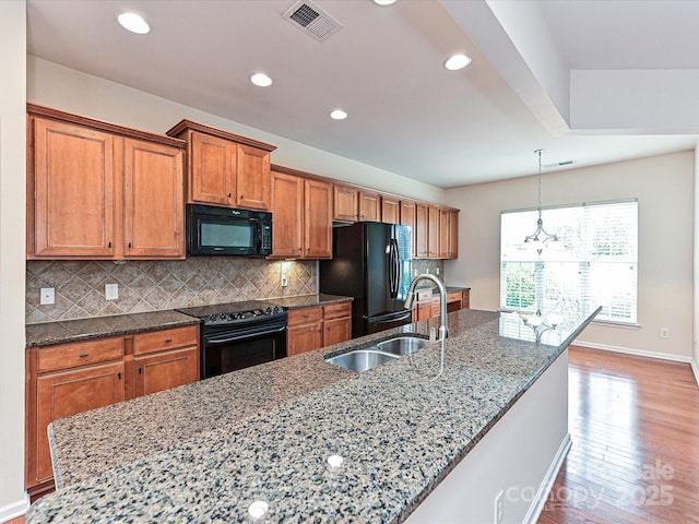 kitchen with light wood-type flooring, brown cabinets, a sink, black appliances, and tasteful backsplash