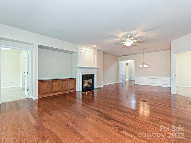 unfurnished living room featuring a fireplace with flush hearth, ceiling fan with notable chandelier, and wood finished floors