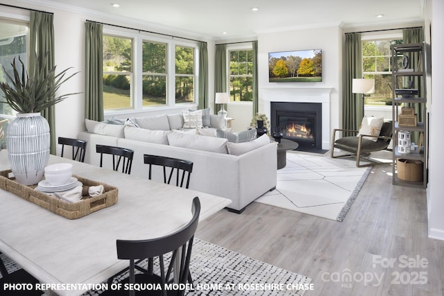 living area featuring recessed lighting, light wood-type flooring, a glass covered fireplace, and crown molding