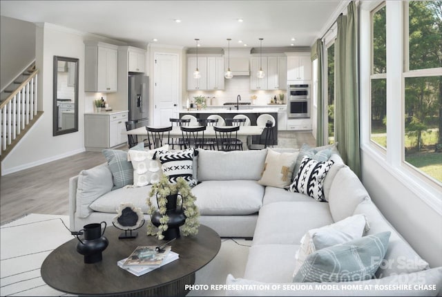 living area featuring light wood finished floors, crown molding, baseboards, stairway, and recessed lighting