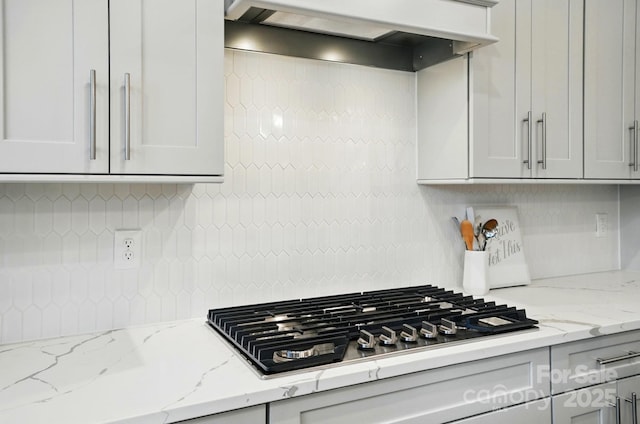 kitchen with stainless steel gas cooktop, light stone countertops, premium range hood, and tasteful backsplash