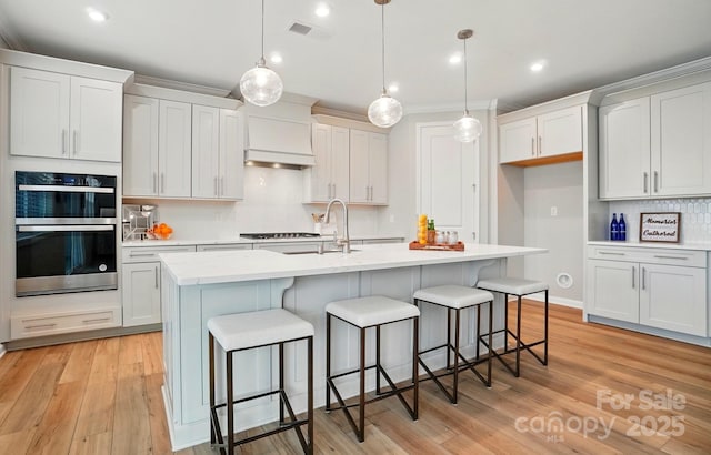 kitchen featuring visible vents, tasteful backsplash, a sink, custom exhaust hood, and light wood-style floors