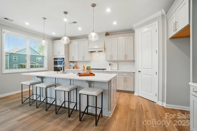 kitchen with visible vents, baseboards, an island with sink, premium range hood, and a kitchen bar