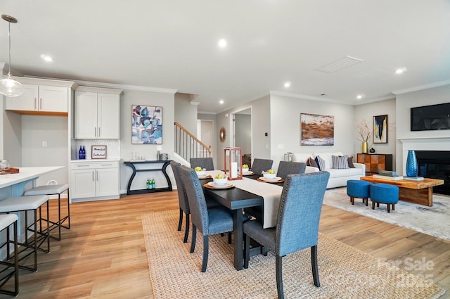 dining space featuring stairs, light wood finished floors, a glass covered fireplace, ornamental molding, and recessed lighting