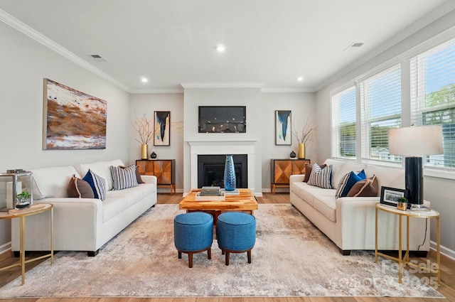 living room featuring visible vents, crown molding, wood finished floors, baseboards, and a glass covered fireplace