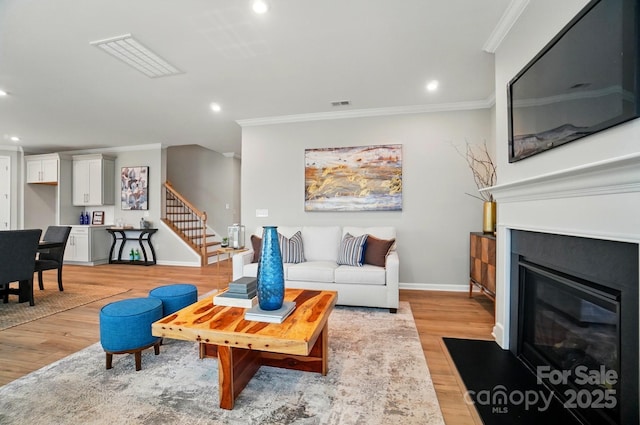 living area with recessed lighting, ornamental molding, light wood-style flooring, and stairway