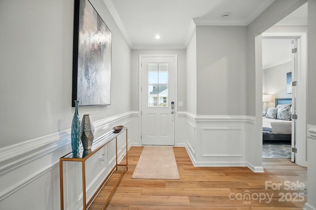 entryway with ornamental molding, wainscoting, and light wood-style flooring