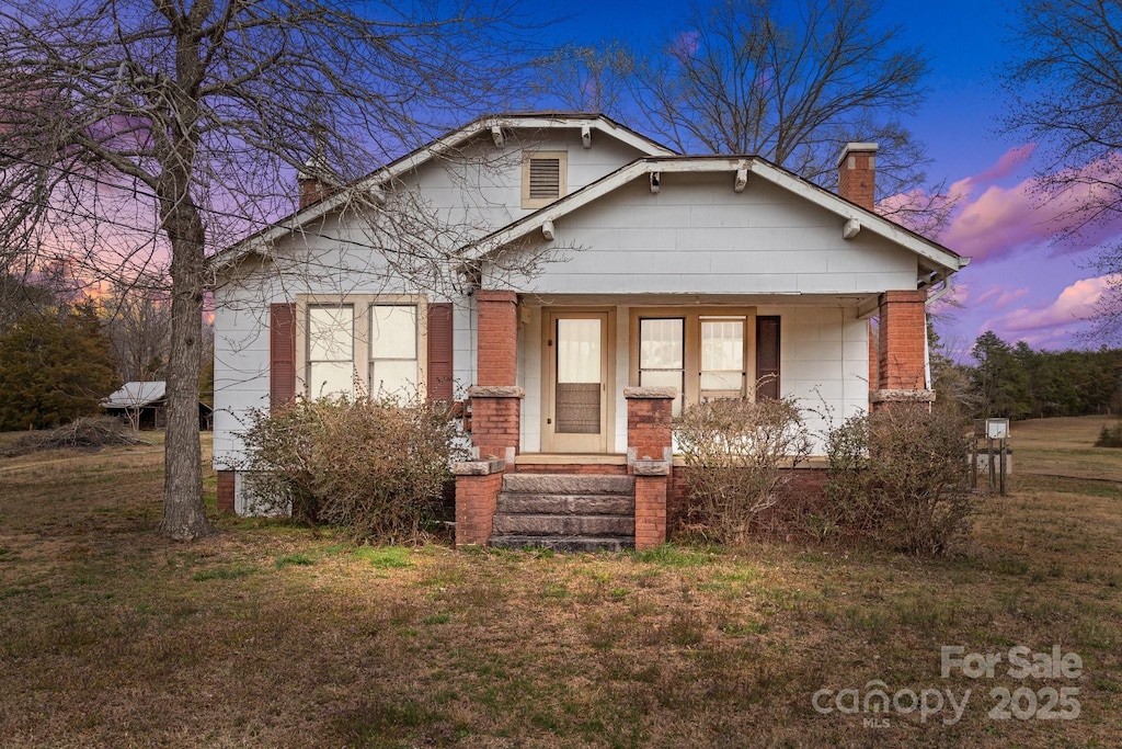 bungalow featuring a yard, brick siding, and a chimney